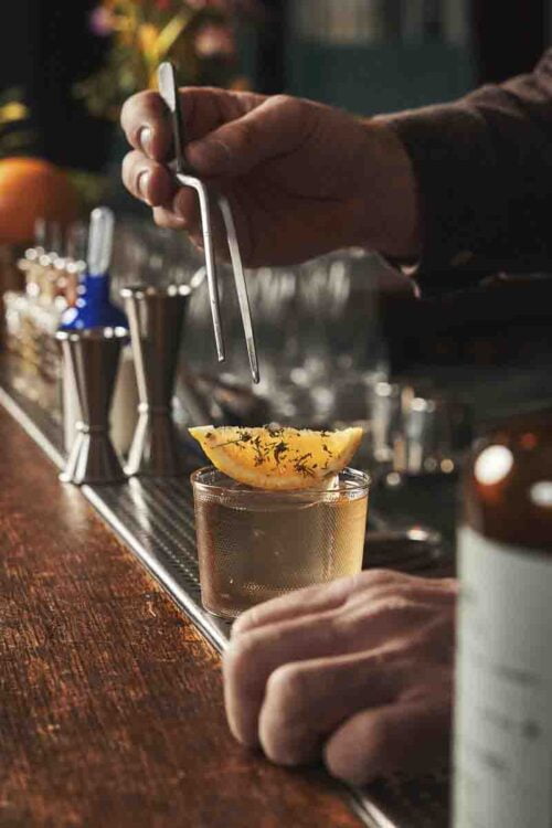 Photo d’un homme qui pose un quartier de citron sur le cocktail servi dans un verre