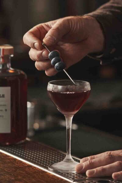 Photo d’un homme qui pose une brochette de myrtilles sur un cocktail servi dans un verre à pied